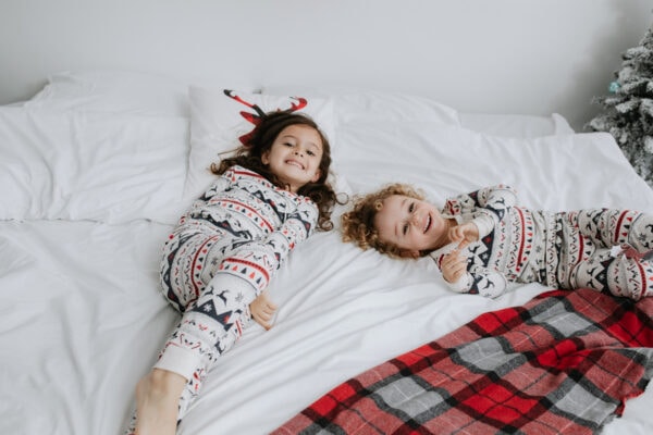 brother and sister in matching christmas pyhamas, on a white bed at their christmas mini photoshoot in bexley