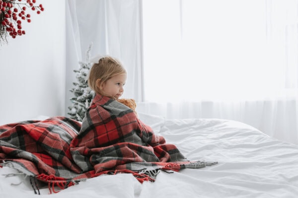 little girl wrapped in a tartan blanket on a white bed at her bexley christmas mini photoshoot