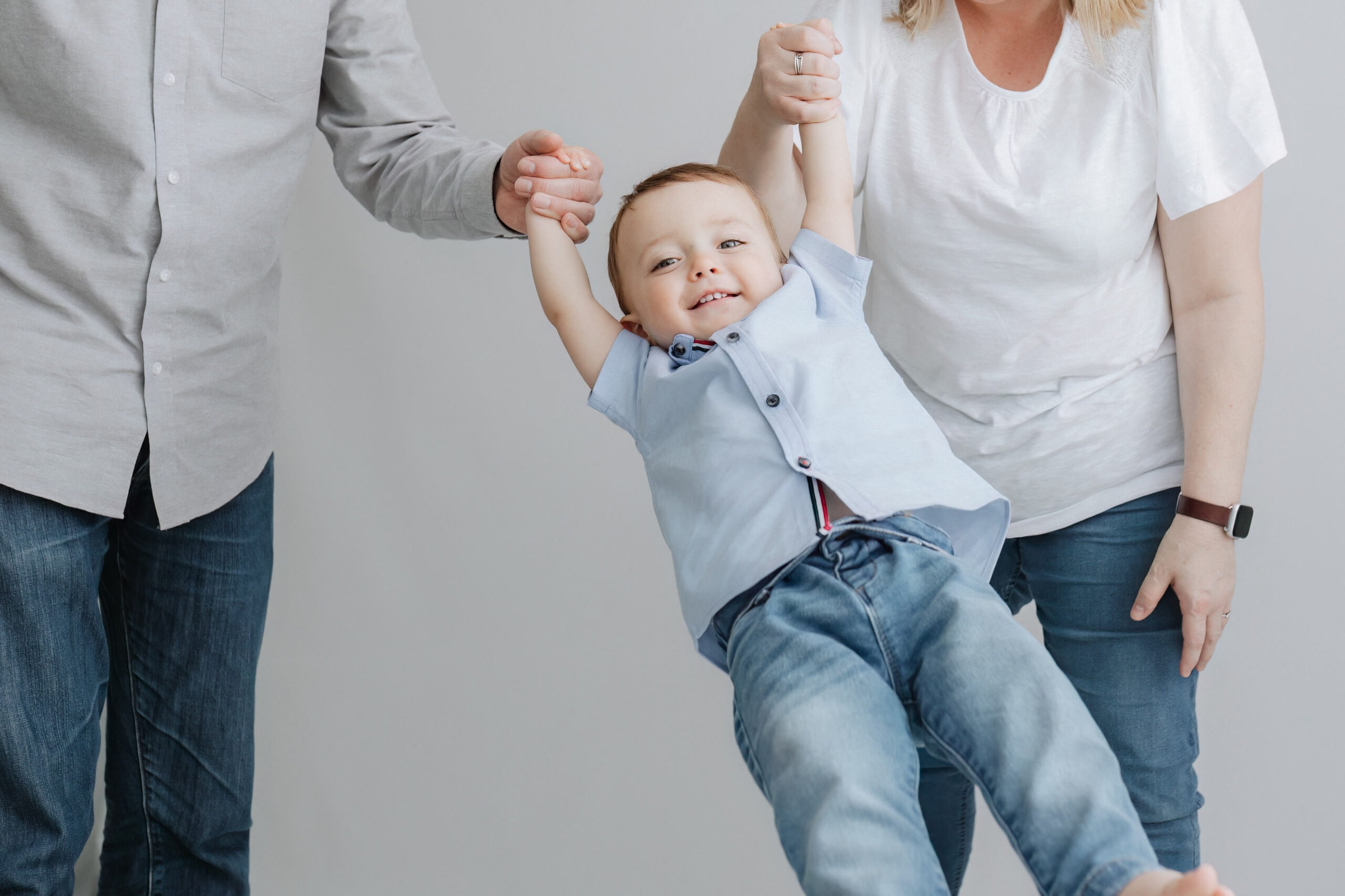 little boy being swung between his parents arms laughing at his older baby photoshoot in bexley kent