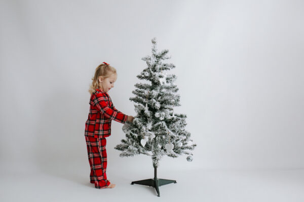 Little girl in Christmas PJs with a single white themed Christmas tree at her Christmas mini photoshoot in Bexley